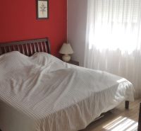 A bedroom in a studio apartment with a red wall, a bed, and two lamps.