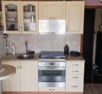 A kitchen in a studio apartment with a kitchen unit, wood decor, and appliances.