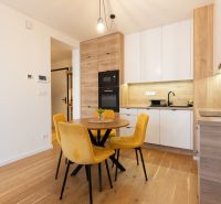 A kitchen in a 2-room apartment with a wooden decor floor and yellow chairs.