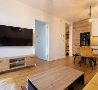 A living room in a two-room apartment with a yellow couch and a wooden decor floor.