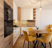 A kitchen in a 2-room apartment with a dining table, yellow chairs, and a wooden decor floor.