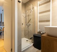 Bathroom with a glass shower enclosure, sink, and floor with a wooden decor in a 2-room apartment.