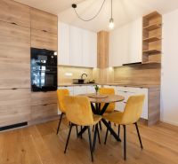 A kitchen in a 2-room apartment with a wooden decor floor and yellow chairs.