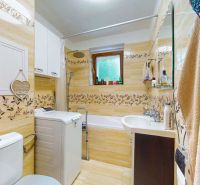 Bathroom with a washing machine and a bathtub in a 2-room apartment, ceramic tiles with a floral pattern.