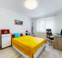 Bedroom in a 2-room apartment with a bed and a desk, wooden decor flooring.