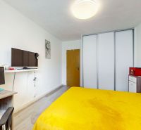 A room with a yellow bedspread, a desk, and a built-in wardrobe in a 2-room apartment.