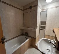 A bathroom in a 3-room apartment with a bathtub, sink, and light tiles.