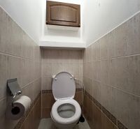A toilet in a 3-room apartment with tiles and a storage cabinet.
