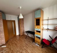 A room in a 3-room apartment with a wooden decor floor, shelves, and a relaxation chair.