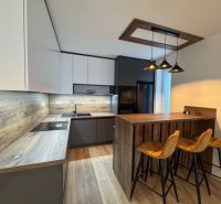 A kitchen in a 2-room apartment with a bar counter, a wooden decor floor, a trio of chairs.