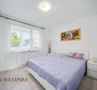 A bright bedroom with wood-patterned flooring and a bed in a three-room apartment.