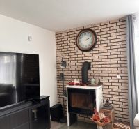 Living room in a family house with a fireplace, brick cladding, and a wooden decor floor.