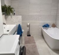A bathroom in a family house with a washing machine, a bathtub, and white tiles on the walls.