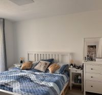 Bedroom in a family house with a bed and a drawer table, light walls and textiles.