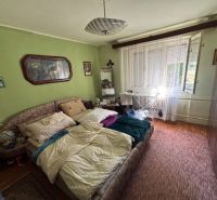 A bedroom in a family house with green walls, a carpet, a bed, and a large window.