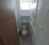Bathroom with toilet and window in a 3-room apartment. Narrow dimensions, white tiles.