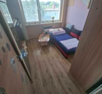 A room in a 3-room apartment with a wood-decor floor and a sofa by the window.