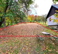 Gardens in Bystré with fallen leaves, a bench, and a house in the background.