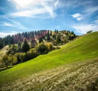Hilly landscape with green meadows and forests in the Banská Štiavnica district, nature illuminated by the sun.