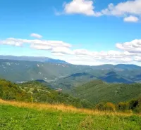 Hilly landscape of agricultural and forest land in Ratkovské Bystré under a blue sky.