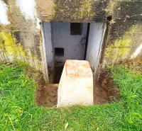 Basement entrance in Malacky with a concrete block and overgrown lawn, Unusual properties.