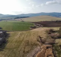 Agricultural and forest lands in Podhorany with diverse colors of fields and low hills.