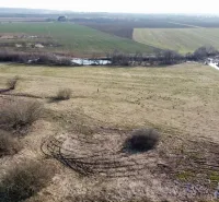 Agricultural and forest land in Podhorany with fields, trees, and grassy areas.
