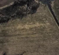 Aerial view of agricultural and forest lands in Podhorany with a river and vegetation.
