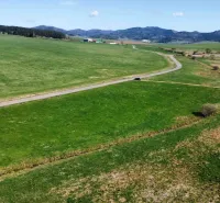 Landscape in Podhorany with agricultural and forest land, a road, and mountains in the background.