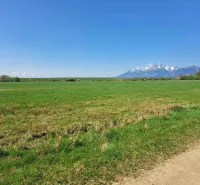 Agricultural and forest lands in Podhorany with a view of snow-covered mountains and a blue sky.