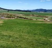 The landscape in Podhorany, agricultural and forest lands with meadows, a road, and surrounding mountains.