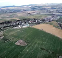 View of agricultural and forest lands in Podhorany surrounded by hills and fields.
