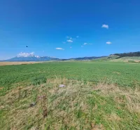 Agricultural and forest land in Podhorany with a panorama of mountains and a blue sky.