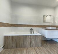 A bathroom with a bathtub, sink, and wooden decor flooring in a family house.