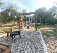 The garden of a family house in Dobroč with a swing, a fireplace, and a trampoline on a stone surface.