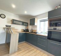 A kitchen in a family house with dark cabinets and a wood-patterned floor.