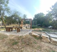The courtyard of a family house in Dobroč with swings, seating, and a trampoline surrounded by greenery.