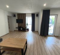 Living room in a family house with wood-patterned flooring, a television, and dark curtains.