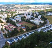 A view of residential buildings and gardens in Zvolen with a lake in the background.