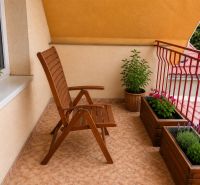 A balcony of a family house with a wooden chair, flowers, and a view of the rooftops in Sereď on Hrnčiarska Street.