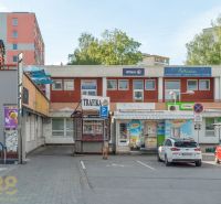 A building in Banská Bystrica with shops and a parking lot, surrounded by greenery and apartment blocks.