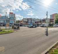 A street in Banská Bystrica with buildings, cars, and passing people.