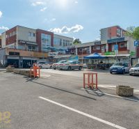 A parking lot with shops and a restaurant in Banská Bystrica, with cars parked around.