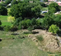 A view of green residential plots in Hronovce, surrounded by trees and grass.
