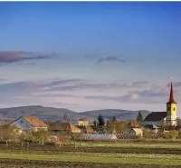 A village with a church in Kamenný Most surrounded by agricultural and forest lands.