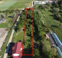 A plot of land in the gardens of the town of Branč, surrounded by greenery and dirt roads.