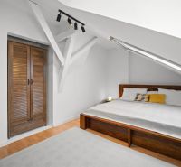 Bedroom with a double bed, sloped ceiling, wood-patterned floor, built-in wardrobe.
