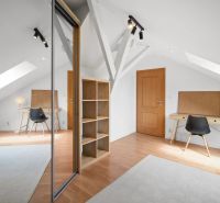 Attic room with a table, black chair, mirrored wardrobe, and wooden decor flooring.