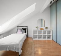 Attic bedroom with a single bed, wooden decor flooring, and storage spaces.