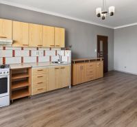 A kitchen in a studio apartment with a wood-patterned floor and light-colored furniture.